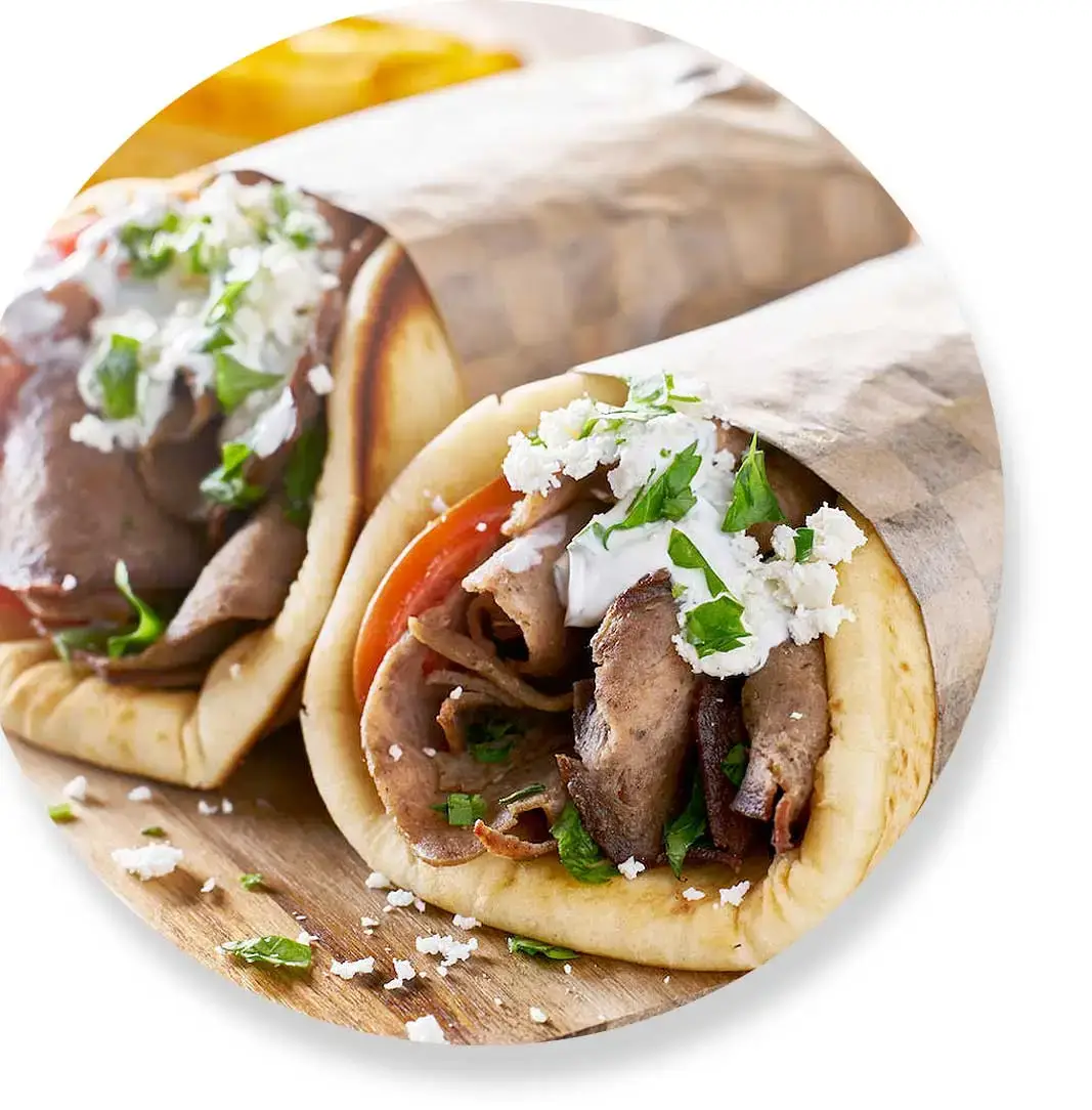 Two gyros wrapped in paper, filled with meat, tomatoes, lettuce, feta cheese, and topped with sauce.